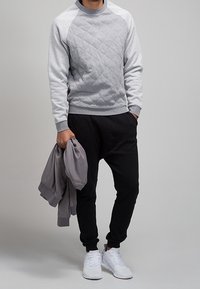 Jasnoszary, pikowany sweter z długim rękawem w kontrastowym kolorze, zestawiony z czarnymi spodniami dresowymi i białymi sneakersami. Casualowy sportowy wygląd.