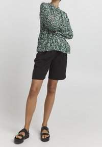 Blusa floreale a maniche lunghe verde, con piccoli fiori bianchi e rosa. Abbinata a pantaloncini neri e sandali con platform neri.