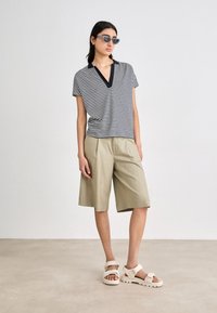 Stripet svart og hvitt kortermet topp med V-hals, sammen med khaki knelange shorts og hvite sandaler med justerbare stropper.