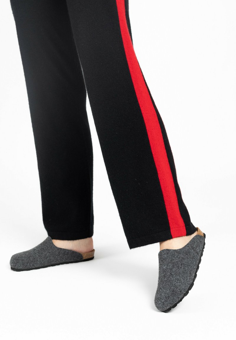 Szare pantofle wsuwane z korkowym akcentem na pięcie. Czarne spodnie mają wyraźny czerwony pasek po boku.