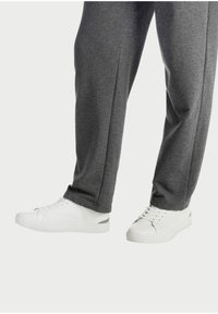Weiße Sneakers mit einem strukturierten Canvas-Obermaterial, flacher Gummisohle und grauen Akzentdetails. Kombiniert mit grauen schmal geschnittenen Sweatpants.