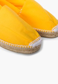 Žluté plátěné espadrilky s kulatou špičkou a bílým prošíváním, s povrchovou úpravou ze juty pro další texturu a kontrast.