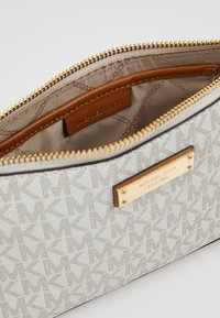 Pouzdro na zip ze šedé látky s vzorem, které má akcenty z pozlaceného kovu a hnědou koženou vnitřní štítek s názvem značky.