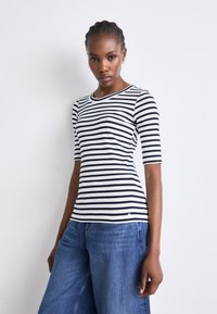 Gestreiftes schwarzes und weißes, tailliertes Oberteil mit Rundhalsausschnitt und kurzen Ärmeln, kombiniert mit weiten blauen Jeans aus Denim.