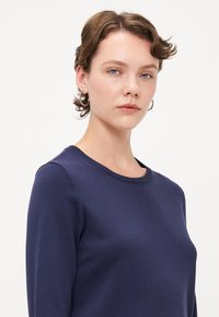 Marineblå genser i fint strikk med rund hals og ribbestrikkede mansjetter. Stoffet ser glatt ut med subtile teksturdetaljer.
