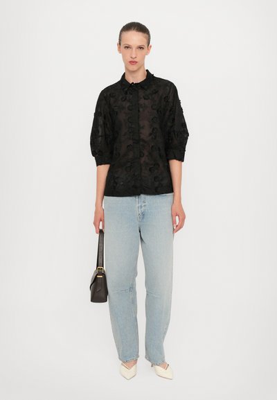 Sort, transparent button-up skjorte med blomstermønster, ballonsleeves. Sættes sammen med lyseblå løse jeans og cremefarvede spidse hæle. Lille sort håndtaske.