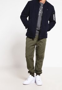 Chamarra bomber acolchada en color navy con cuello de canalé, sudadera gris debajo, pantalones oliva ajustados y zapatillas blancas.