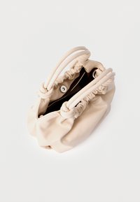 Beige stoffen handtas met een geplooid ontwerp, twee afgeronde handgrepen, een magnetische drukknoopsluiting en een gestructureerd oppervlak. De binnenkant is donker.