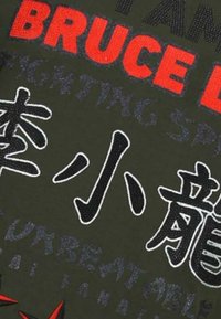 Groene stof met gedurfde rode en zwarte tekst met Chinese karakters, geaccentueerd door rode stergrafieken. Het ontwerp bevat verschillende lettertypes.