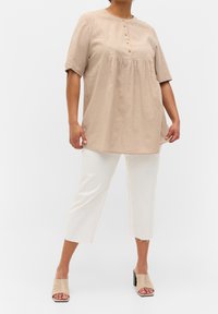 Beige linen tunic with short sleeves and a rounded neckline, featuring a button placket and gathered detail. Paired with white cropped pants and beige mules.