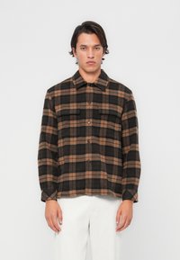 Brown and black plaid shirt, made of soft fabric, featuring a button-up front, two chest pockets, and long sleeves.