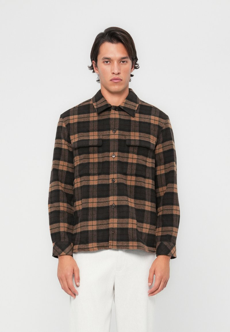 Brown and black plaid shirt, made of soft fabric, featuring a button-up front, two chest pockets, and long sleeves.