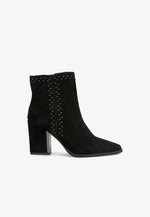 Zwarte suède enkellaars met puntige neus, studs langs de zijkanten en een chunky hak met een metalen accent.