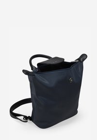 Bolso azul marino con un acabado mate, que presenta un asa superior texturizada en negro, un cierre de cremallera y un detalle decorativo de botón a presión.