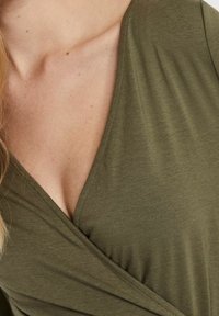 Oliivinvihreä kietaisupaita, valmistettu pehmeästä kankaasta, jossa on syvä V-kaula-aukko ja rintamuksen kerätty rakenne lisäyksityiskohtana.