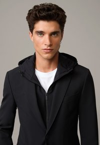 Czarna kurtka z kapturem, zapinana na zamek, z kołnierzykiem i białą koszulką pod spodem. Gładki materiał o dopasowanym kroju i subtelnych detalach.