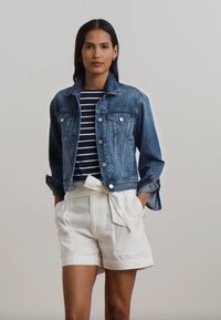 Τζάκετ από τζιν με καρφίτσες, με κλασική γραμμή και ανοιχτό μπλε χρώμα. Ριγέ μπλούζα σε ναυτικό μπλε και λευκό από κάτω, συνδυασμένη με λευκά σορτς ψηλής μέσης.