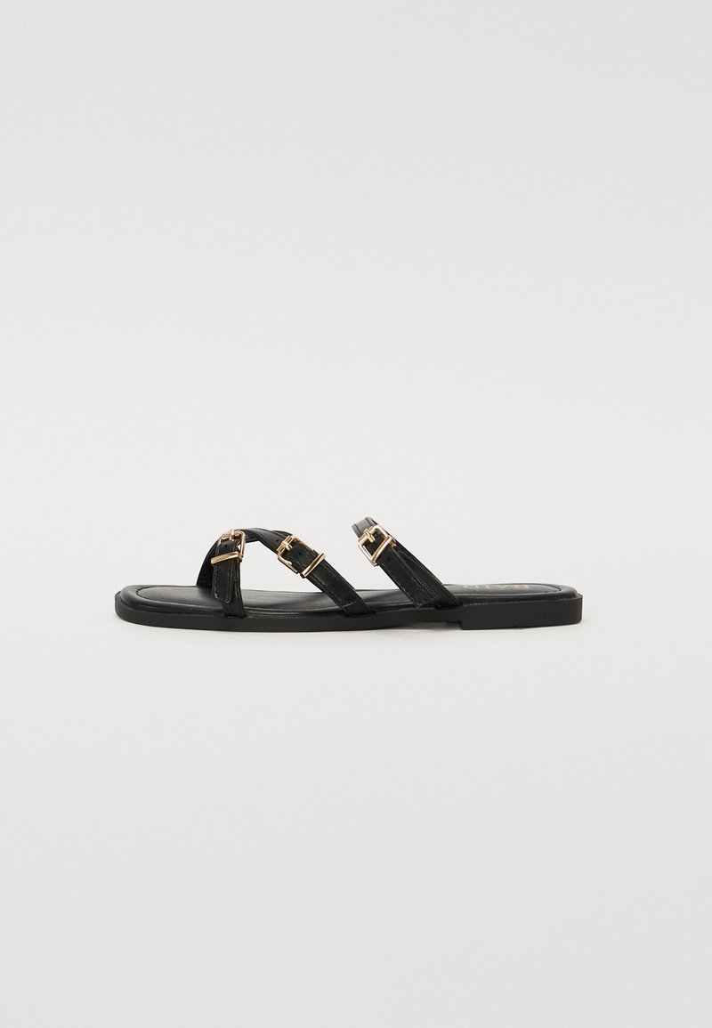 Zwarte platte sandalen met drie banden en gouden gespen. Gladde leren materiaal en een minimalistische platte zool.