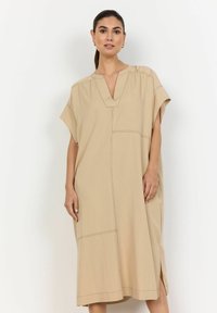 Beige jurk tot de knie met een V-hals en korte mouwen. Bevat horizontale en verticale stikdetails, zijsplitten en een losse pasvorm.