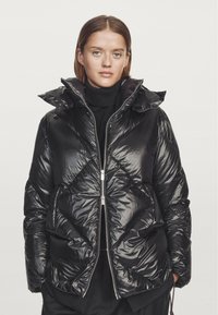 Black padded jacket made from shiny nylon material. Features a high collar, zipper front, and diamond quilted pattern with side pockets.