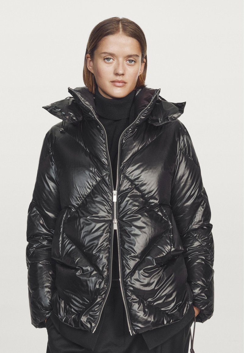 Black padded jacket made from shiny nylon material. Features a high collar, zipper front, and diamond quilted pattern with side pockets.