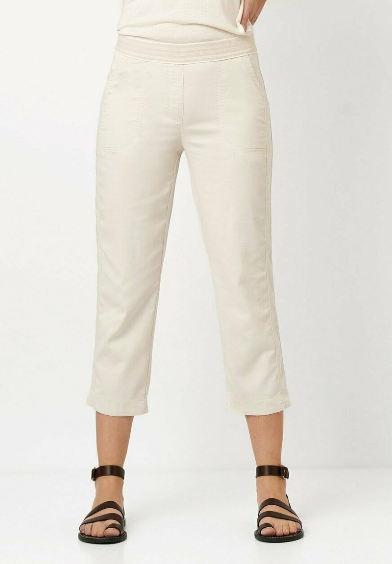 Beige Cropped-Hosen mit glatter Textur, elastischem Bund und gestickten Fronttaschen, kombiniert mit schwarzen Riemchensandalen.