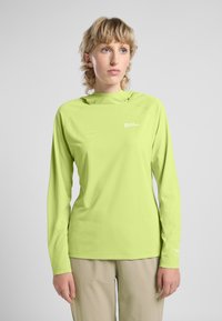 Helles grünes Langarmshirt mit weicher Textur, ausgestattet mit einer Kapuze und einem kleinen Logo auf der Brust. Kombiniert mit beigen Hosen.