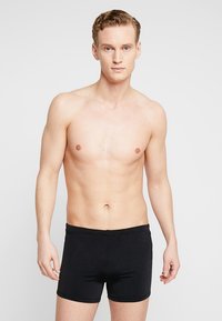 Fekete boxer alsónadrág rugalmas anyagból, fitted dizájnnal és puha derékkal. A modellen nincs póló, látható a törzse.