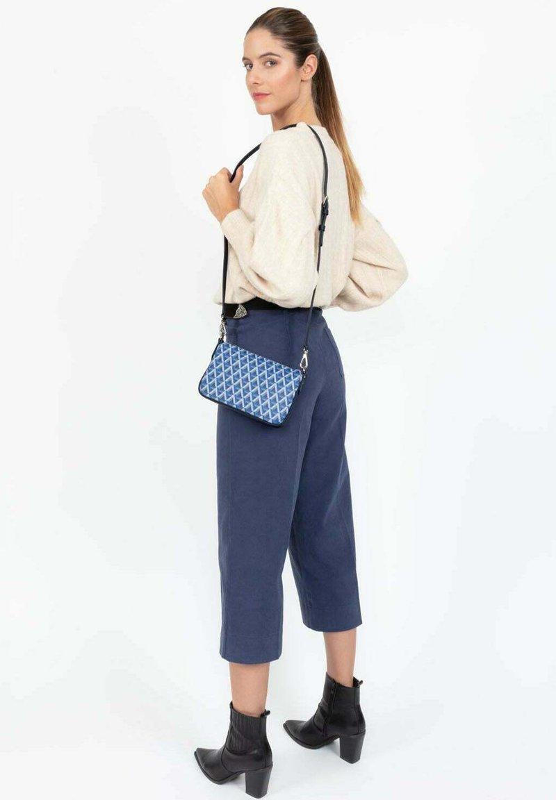 Sac en bandoulière bleu à motif avec fermeture éclair, présentant un design géométrique, une sangle noire réglable et des accents en métal argenté.