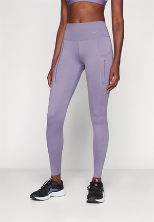 Lila sport leggings magas derékkal, oldalsó zsebekkel és sima, rugalmas anyagból. Fekete sportcipővel párosítva.