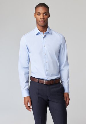 Light blue long-sleeve dress shirt with a button-down collar, featuring a smooth cotton fabric and a tailored fit. Dark brown leather belt accents.