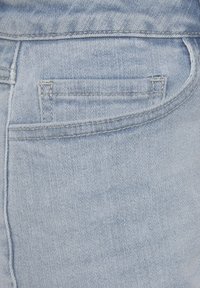 Tela de mezclilla azul claro que muestra un bolsillo trasero con costura superior y una textura suave, con un sutil patrón descolorido.