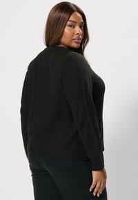 Svart stickad tröja med en strukturerad väv, utrustad med långa ärmar och rundad halsringning, i kombination med mörka jeans.