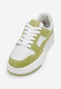 Zapatilla de ante verde lima y cuero blanco con puntera perforada, cordones blancos y suela de goma texturizada. Logo en relieve en la lengüeta.