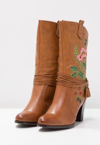 Braune Stiefeletten aus Kunstleder mit einem gestapelten Absatz, die mit floraler Stickerei in Rosa und Grün sowie dekorativen Wickeldetails versehen sind.