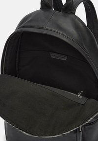 Czarny skórzany plecak z gładką powierzchnią, z zamykaną na zamek komorą oraz miękką, teksturowaną podszewką wnętrza. Regulowane paski.