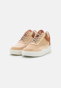 Une paire de baskets en daim beige et rouille avec des lacets beiges et des semelles blanches épaisses sur un fond blanc.