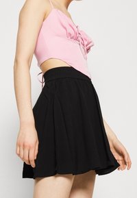 Un haut cropped rose avec un détail de nœud à l'avant associé à une jupe évasée noire avec une taille élastique et une texture de tissu douce.