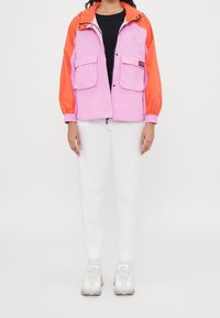 Colorful jacket featuring a pink body and orange sleeves, made of smooth material, with two front pockets and a zip closure.