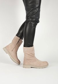 Botas de tobillo de ante beige con punta redonda y cremallera lateral. Presentan una superficie texturizada y una suela resistente de color claro.