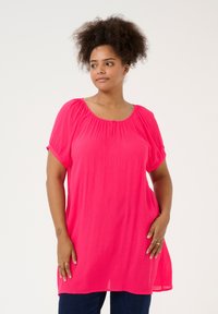 Blusa rosa con scollo a barca, maniche corte arrotolate e vestibilità rilassata. Presenta un tessuto leggero e testurizzato e un'orlo leggermente più lungo.