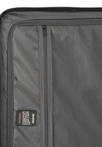 Interno di una valigia grigia in soft-shell con scomparti con zip, tasche in rete e un'etichetta del marchio nera con testo bianco, tessuto testurizzato.