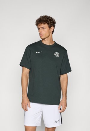Mørkegrøn Nike t-shirt med korte ærmer, rund hals og cirkulært logo på brystet. Model iført hvide shorts med sort accent.