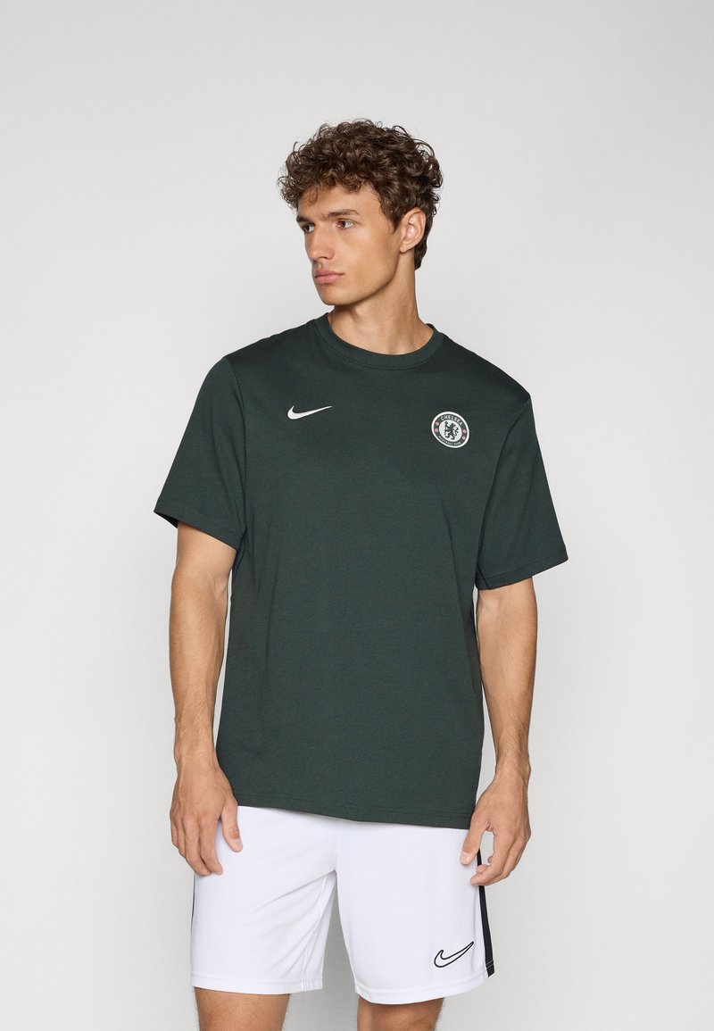 Donkergroen Nike T-shirt met korte mouwen, ronde hals en een cirkelvormig logo op de borst. Model draagt witte shorts met een zwart accent.