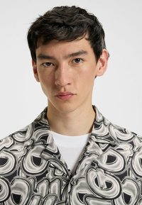 Camicia a maniche corte con bottoni in un motivo marmorizzato nero e bianco, caratterizzata da un colletto aperto e un fit rilassato con una leggera lucentezza.
