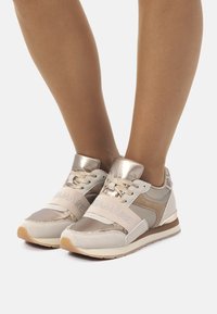 Sneaker beige con accenti metallici, caratterizzate da un mix di materiali scamosciati e in rete, design strutturato e una larga fascia con marchio.