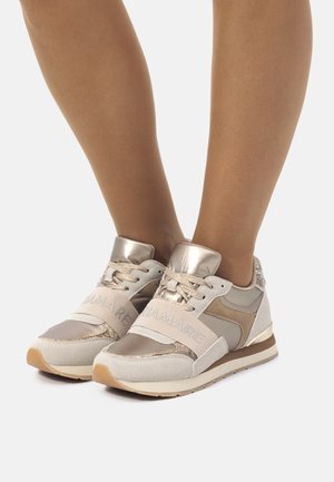 Baskets beiges avec des accents métalliques, présentant un mélange de matériaux en daim et en mesh, un design structuré et une large sangle avec un logo.