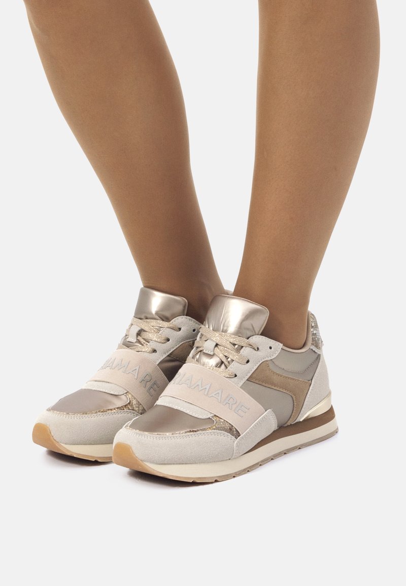Sneaker beige con accenti metallici, caratterizzate da un mix di materiali scamosciati e in rete, design strutturato e una larga fascia con marchio.
