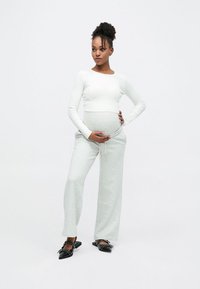 Light gray, loose-fitting joggers paired with a white long-sleeve top; model cradling her pregnant belly; black, pointed-toe flats.