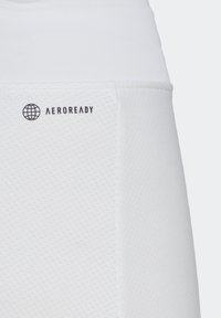 Pantalones cortos deportivos blancos con un patrón texturizado, que cuentan con un logotipo AEROREADY en negro, ubicado en la parte superior izquierda.
